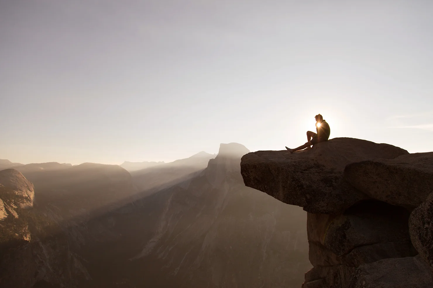 man sitting on the edge of the cliff overlooking beautiful mountain tops